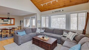 A spacious living room with a large gray sectional sofa, a wooden coffee table, and a dining area with a wooden table and chairs. - Modern Mountain Getaway at Loon (Lincoln)