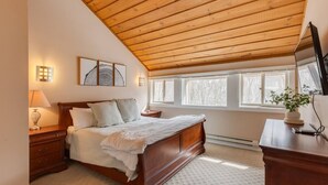 A bedroom with a wooden ceiling, a bed, bedside tables, a lamp, artwork, a potted plant, and a window. - Modern Mountain Getaway at Loon (Lincoln)