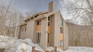 A wooden cabin with a sloped roof, a chimney, and a small porch with steps leading to the entrance. - Modern Mountain Getaway at Loon (Lincoln)