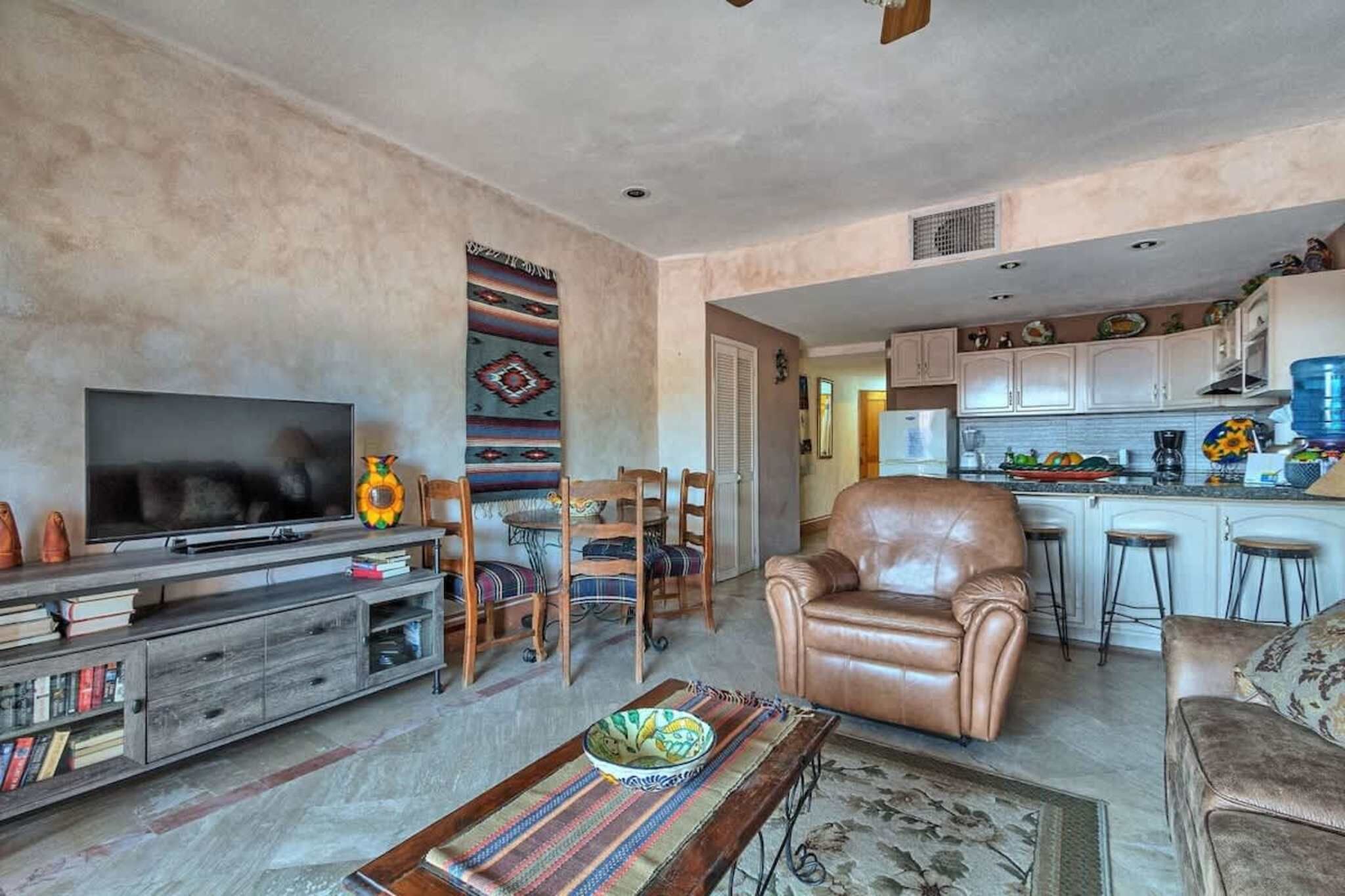 A living room with a TV, leather sofa, and a dining area with chairs.