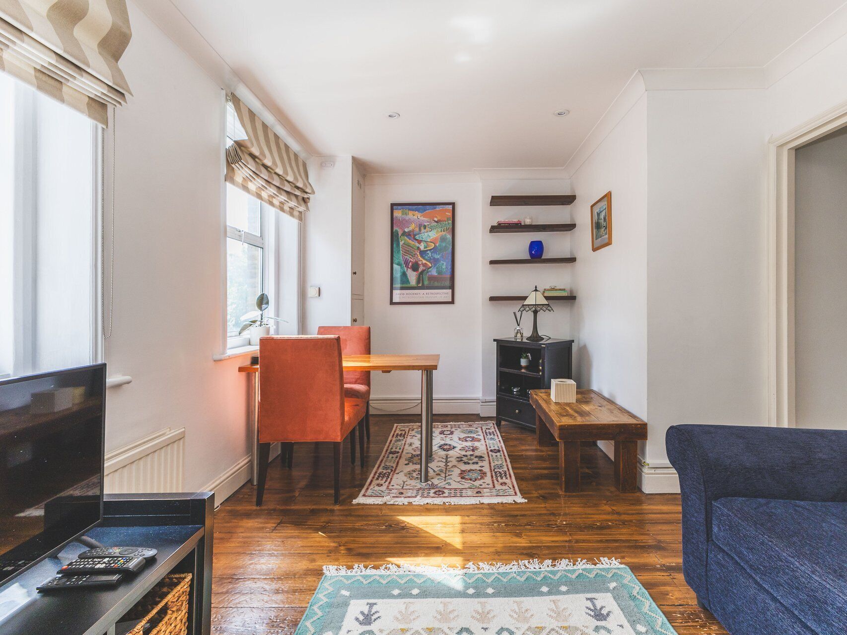 A living room with a TV, sofa, wooden floor, and a dining area with a table and chairs.