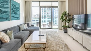 A modern living room with a sofa, coffee table, TV, and large windows. - Stylish 1BR with Private Beach Access (Dubai)