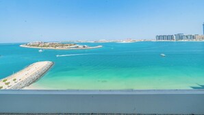 A coastal view with clear turquoise waters, a sandy beach, and distant buildings. - Stylish 1BR with Private Beach Access (Dubai)