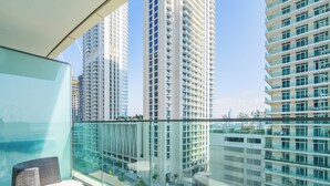 A balcony with wicker furniture, a glass railing, and a view of high-rise buildings. - Stylish 1BR with Private Beach Access (Dubai)