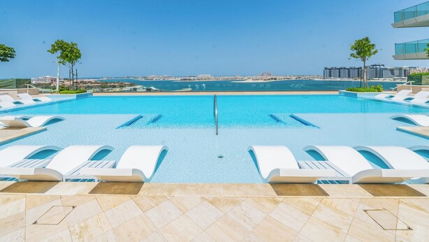 A pool with lounge chairs, a clear view of the sea, and a distant cityscape. - Stylish 1BR with Private Beach Access (Dubai)