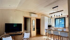 Una sala de estar moderna con televisor de pantalla plana, sillas de mimbre, una mesita y una cocina con barra y taburetes.