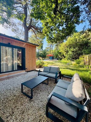 A modern outdoor seating area with a table and two sofas, surrounded by gravel and greenery. - N&L Signature - Ô Lodge (Mornas)