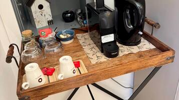 A wooden tray with a coffee maker, jars, and mugs on a metal stand in a room with a white wall and a door.