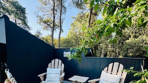 A deck with two Adirondack chairs labeled 'L'AIR DU LARGE' and a small table, surrounded by a rope barrier and trees.