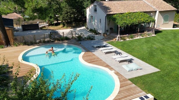 A swimming pool with a wooden deck, lounge chairs, and a house in the background.