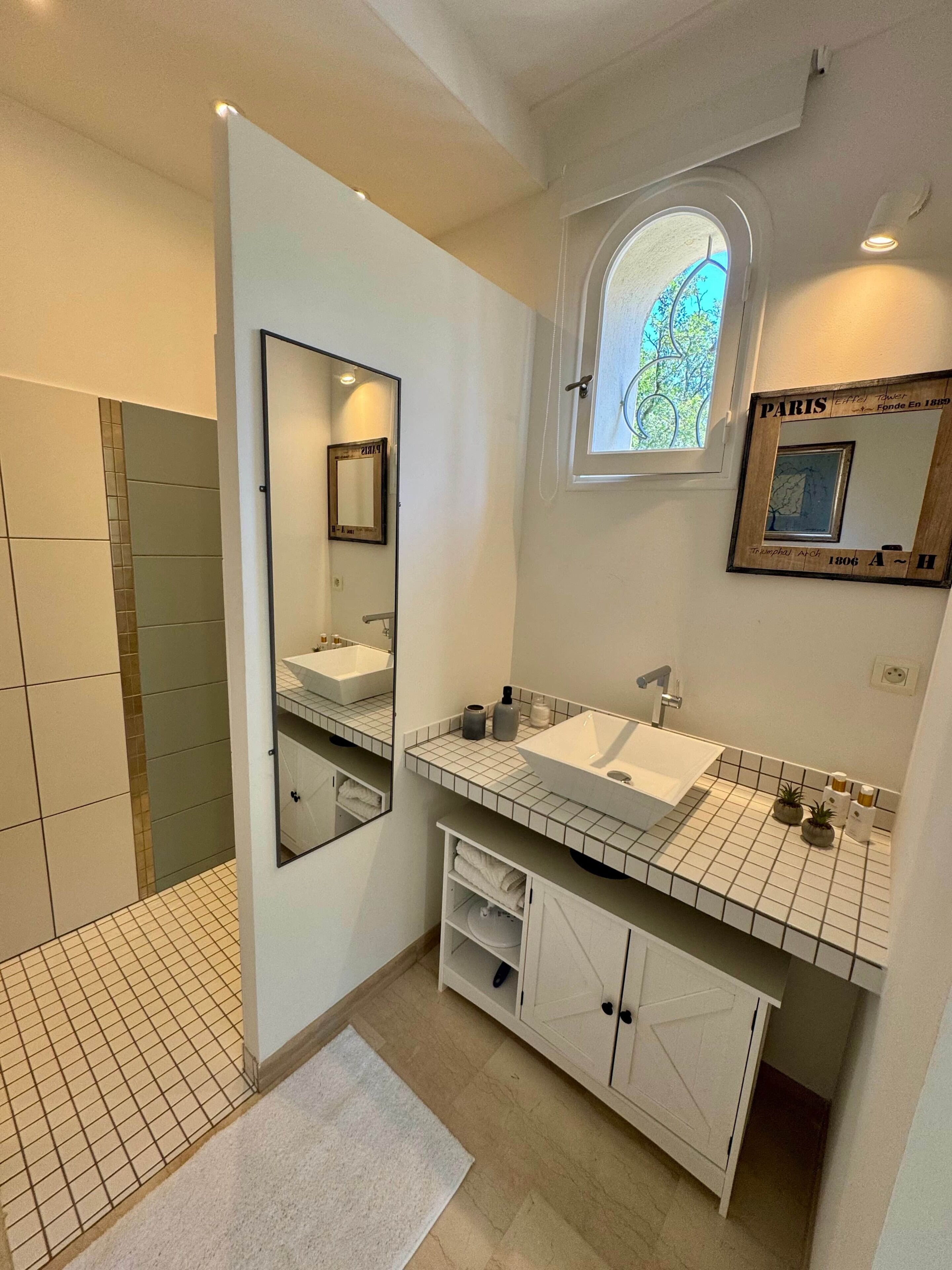 A modern bathroom with a large mirror, two sinks, a window, and a tiled floor.
