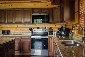 Eine Küche mit Holzausbau, Edelstahlgeräten, Granitabdeckungen und einem eingebauten Backofen.