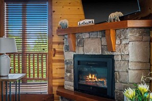 Ein Kamin aus Stein mit einem Fernseher darüber, ein Holztisch mit einer Lampe und ein Fenster mit Jalousien.