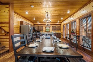 Interior de madera con una larga mesa de comedor lista para una comida, armarios de cocina y una escalera.