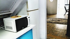 Une cuisine avec un four à micro-ondes posé sur un plan de travail bleu, un réfrigérateur blanc et un sol carrelé.