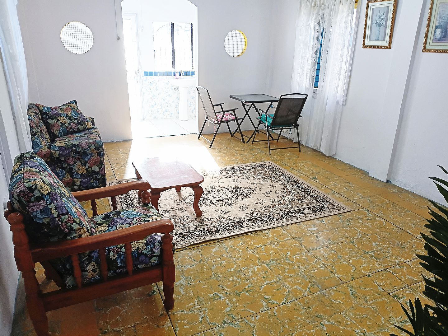 Una sala de estar con un sofá de madera, una mesita pequeña y un tapete estampado.