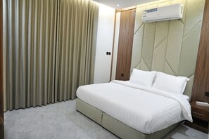 A hotel room with a bed, curtains, an air conditioning unit, and a nightstand.