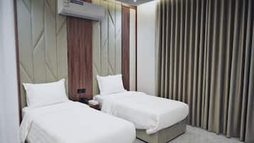 A hotel room with two beds, a wall-mounted air conditioner, and a curtain on the window.