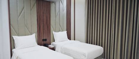 A hotel room with two beds, a wall-mounted air conditioner, and a curtain on the window.