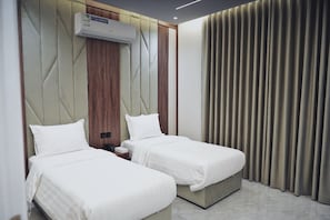 Ein Hotelzimmer mit zwei Betten, einer Wandklimaanlage und einem Vorhang am Fenster.