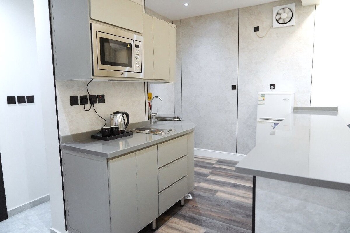 A modern kitchen with a built-in microwave, a kettle, and a refrigerator.