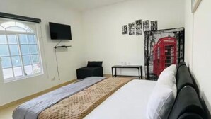 A hotel room with a bed, a TV, a window, and a wall with posters.