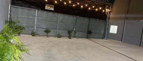 Un espacio al aire libre con piso de concreto, cercado de metal y luces colgantes.