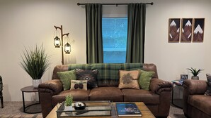 Ein Wohnzimmer mit einem braunen Ledersofa, einem Holztisch und einem Fenster mit grünen Vorhängen.