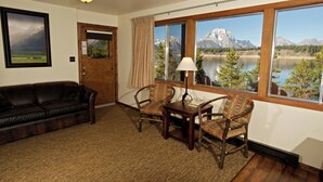 A room with a large window, a wooden door, a leather sofa, two patterned chairs, a small table, and a lamp.