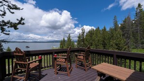 A deck with chairs and a table overlooking a lake with trees and mountains in the background.