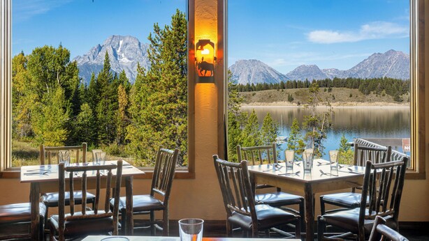 A dining area with tables and chairs, large windows with mountain views, and a decorative wall light.