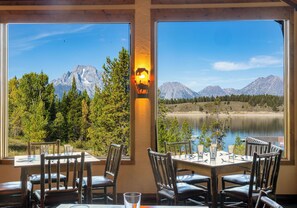 Comedor con mesas y sillas, amplias ventanas con vistas a la montaña y una lámpara de pared decorativa.
