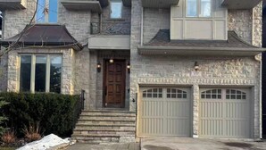 Une maison à deux étages avec une façade en pierre, une porte d’entrée, deux portes de garage et une allée.