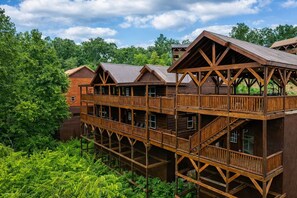 A multi-story wooden building with balconies and a natural forest backdrop. - Luxe Cabin w/ Pool, Game Room, Hottub - Sleeps 26 (Sevierville)