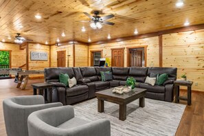 A log cabin interior with a leather sectional sofa, a coffee table, and a game room sign. - Luxe Cabin w/ Pool, Game Room, Hottub - Sleeps 26 (Sevierville)