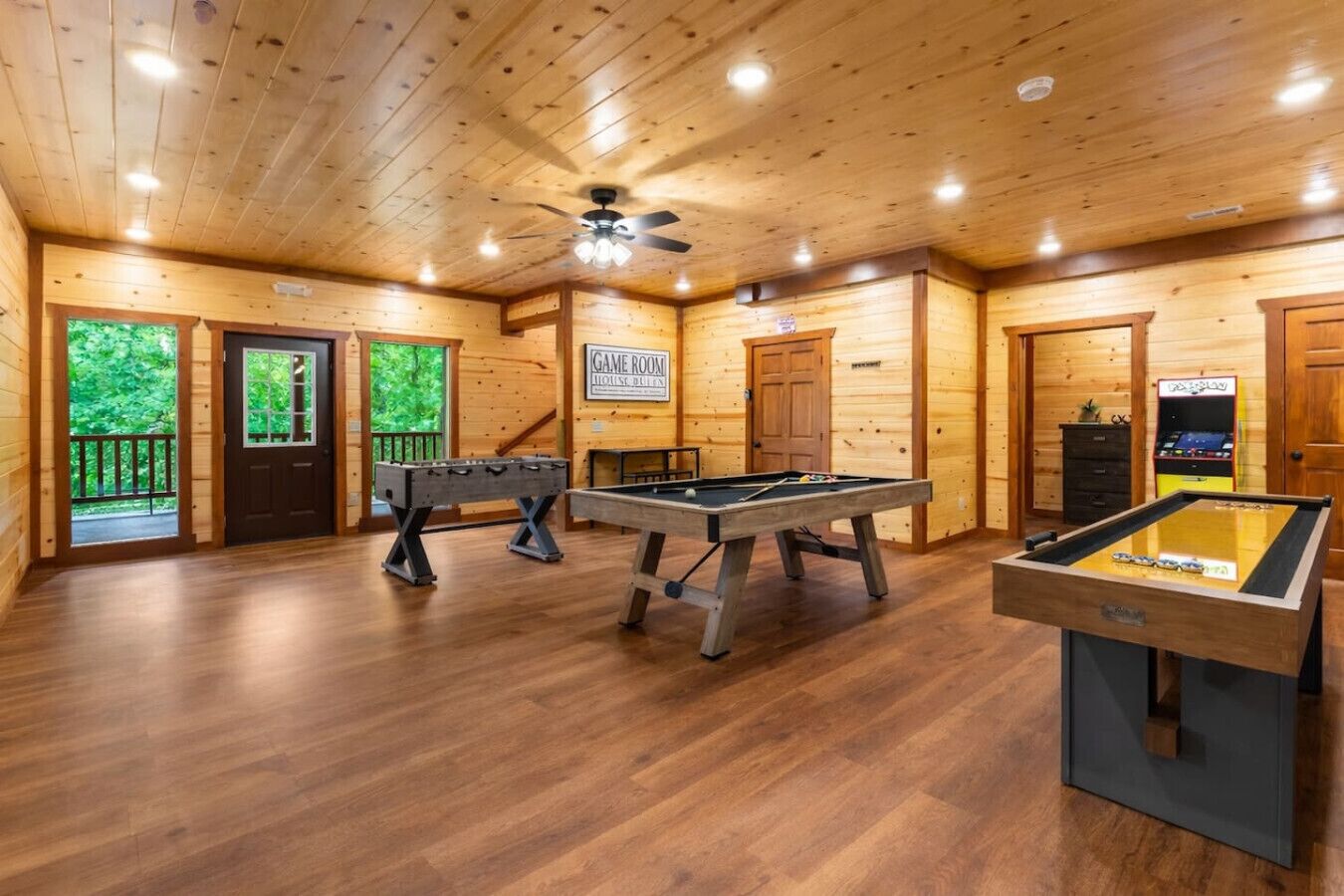 Une pièce au plancher en bois, équipée de deux tables de baby-foot, d’une table de billard et d’une enseigne indiquant qu’il s’agit d’une salle de jeux.