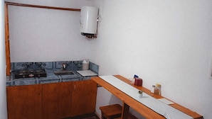 Une petite cuisine équipée d’un évier, d’une cuisinière et d’un chauffe-eau blanc fixé au mur.