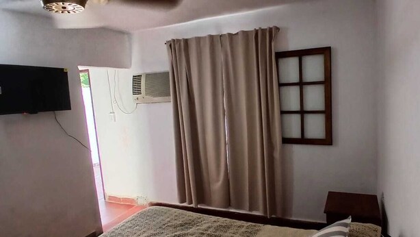 Une chambre avec un lit, une fenêtre avec des rideaux, un climatiseur fixé au mur et un téléviseur.