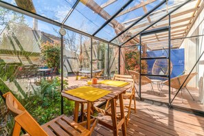 Eine verglaste Terrasse mit Holzmöbeln und Blick auf den Garten.