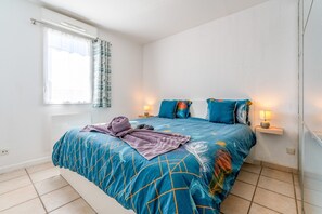 Un dormitorio con cama, dos lámparas de noche, una ventana con cortinas y una toalla sobre la cama.