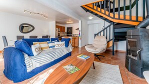 Una sala de estar con sofá, mesa de centro, sillón, chimenea y escalera.