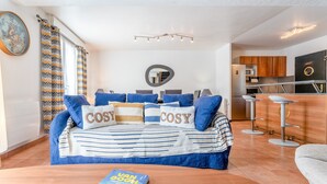 Una sala de estar moderna con sofá cama, una mesa de centro, un libro, una zona de cocina y una mesa de comedor.