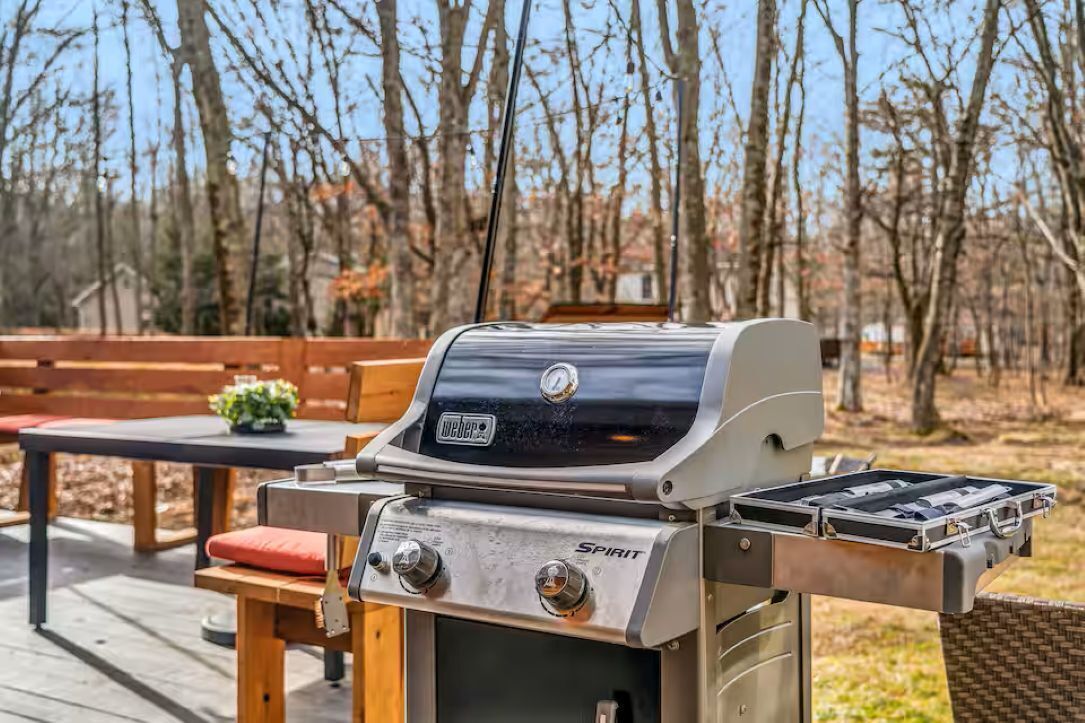 A Weber Spirit grill with a side burner, set on a wooden deck with a table and chairs.