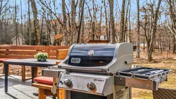 A Weber Spirit grill with a side burner, set on a wooden deck with a table and chairs.