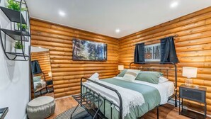 Camera da letto in una baita di legno con un letto, un tavolino, una sedia, uno specchio e un quadro appeso al muro.
