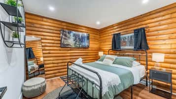 A log cabin bedroom with a bed, a small table, a chair, a mirror, and a painting on the wall.