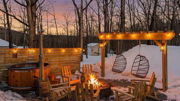 Eine Holzterrasse mit Feuerstelle, Sitzgelegenheiten im Freien und einer Pergola mit Beleuchtung.