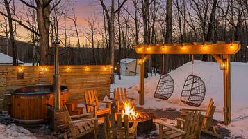 A wooden deck with a fire pit, outdoor seating, and a pergola with lights.