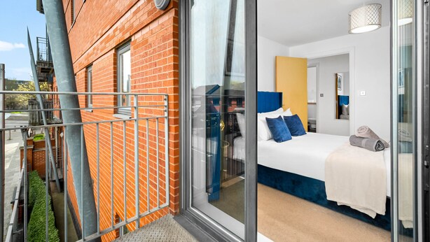 Ein modernes Hotelzimmer mit Glastür, einem Bett mit blauer Bettwäsche, einem weißen Kopfteil und einem großen Fenster.