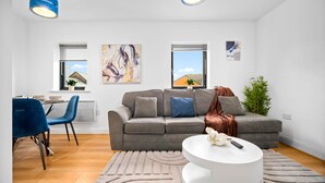 Ein modernes Wohnzimmer mit einem grauen Sofa, blauen Sesseln, einem weißen Couchtisch und Bildern an den Wänden.